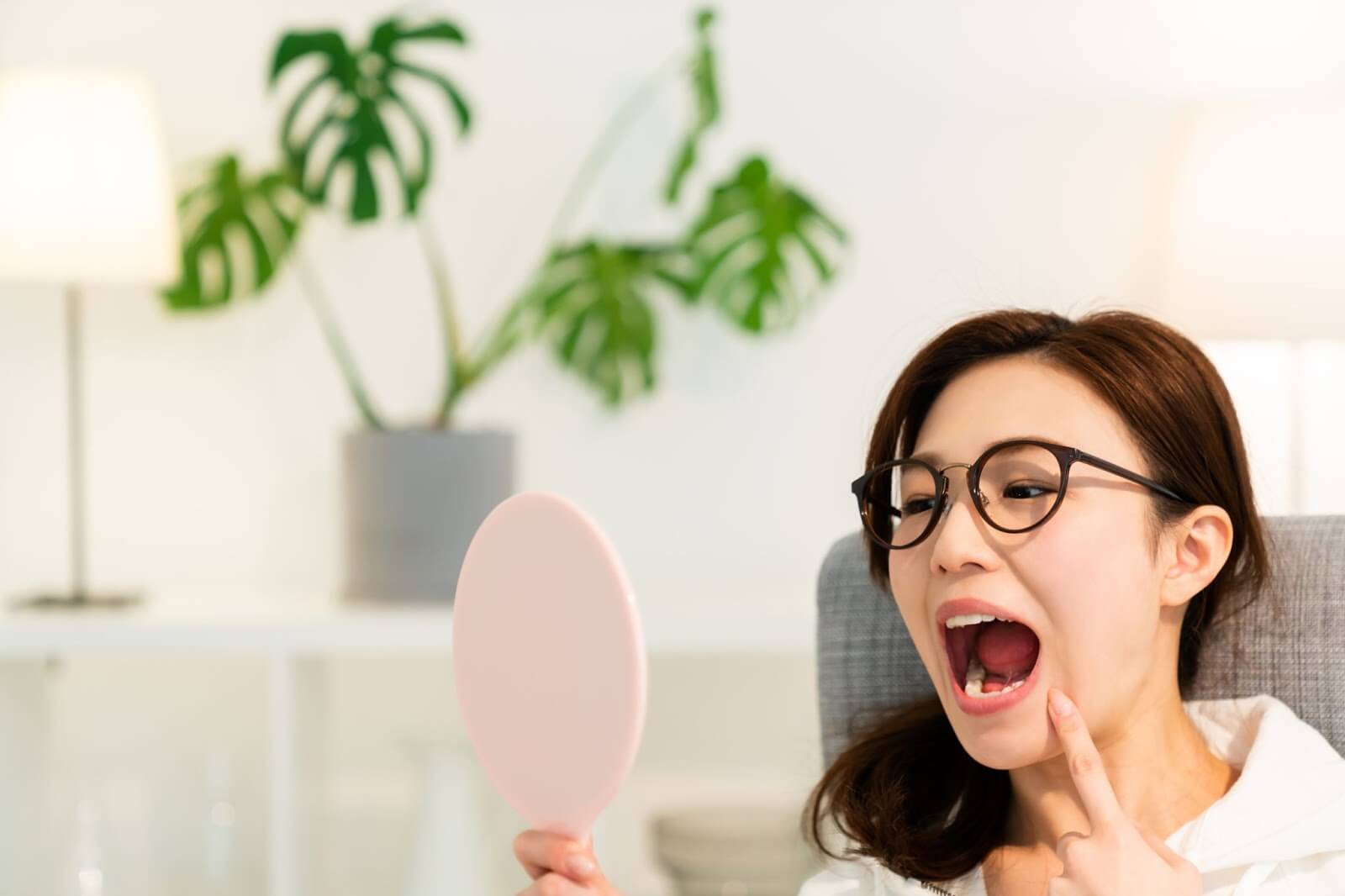 a woman looking at her teeth in a hand held mirror