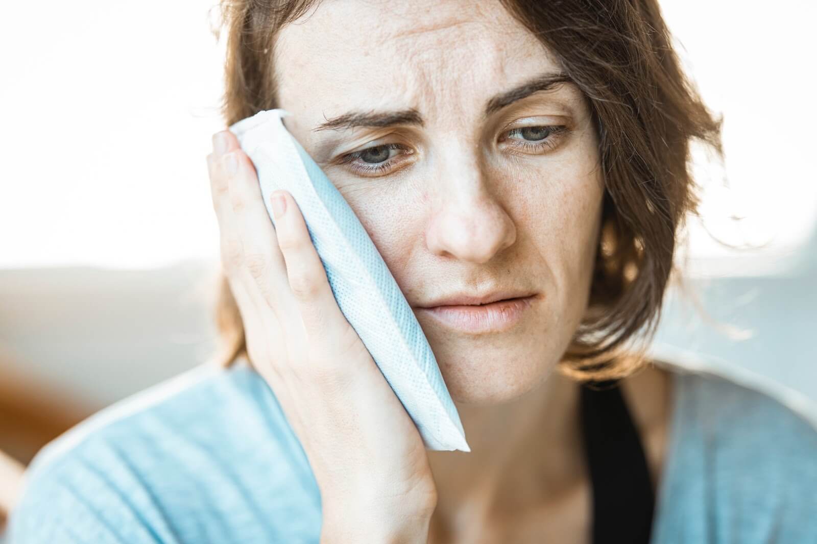 a woman holding a cloth to her cheek appearing to be in pain
