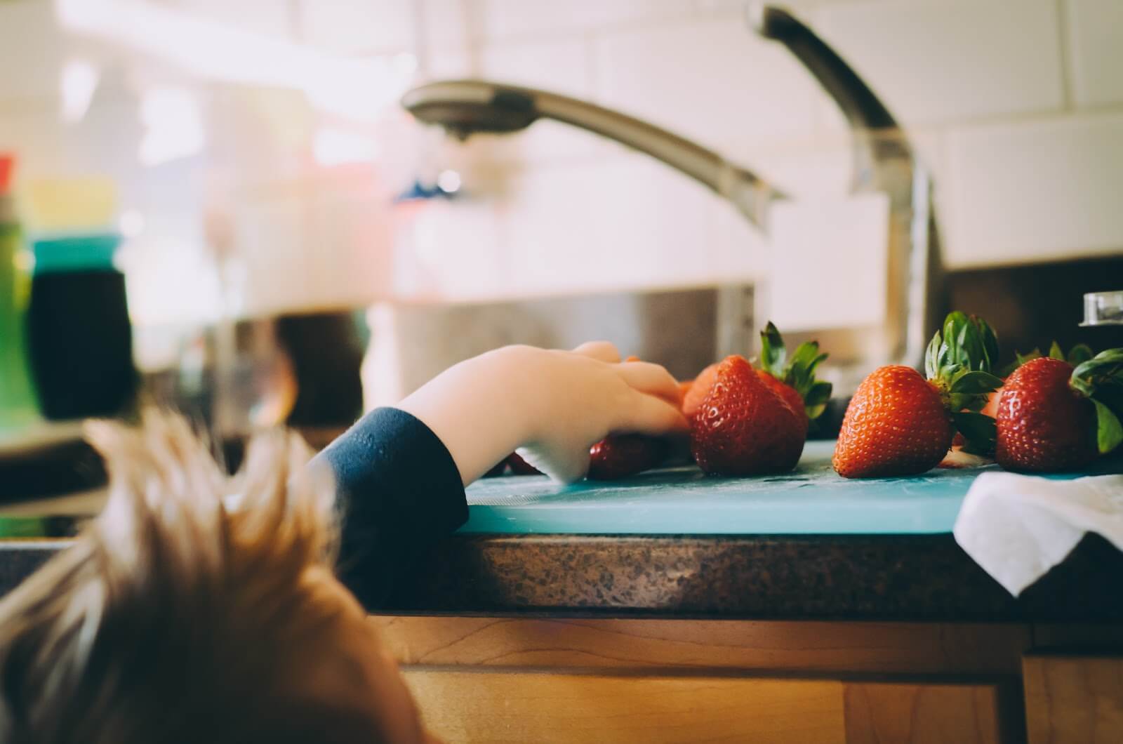 a small child reaching up to grab some strawberries off the counter