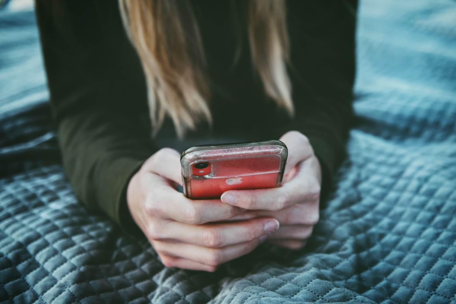 a female laying on a bed and holding her cell phone