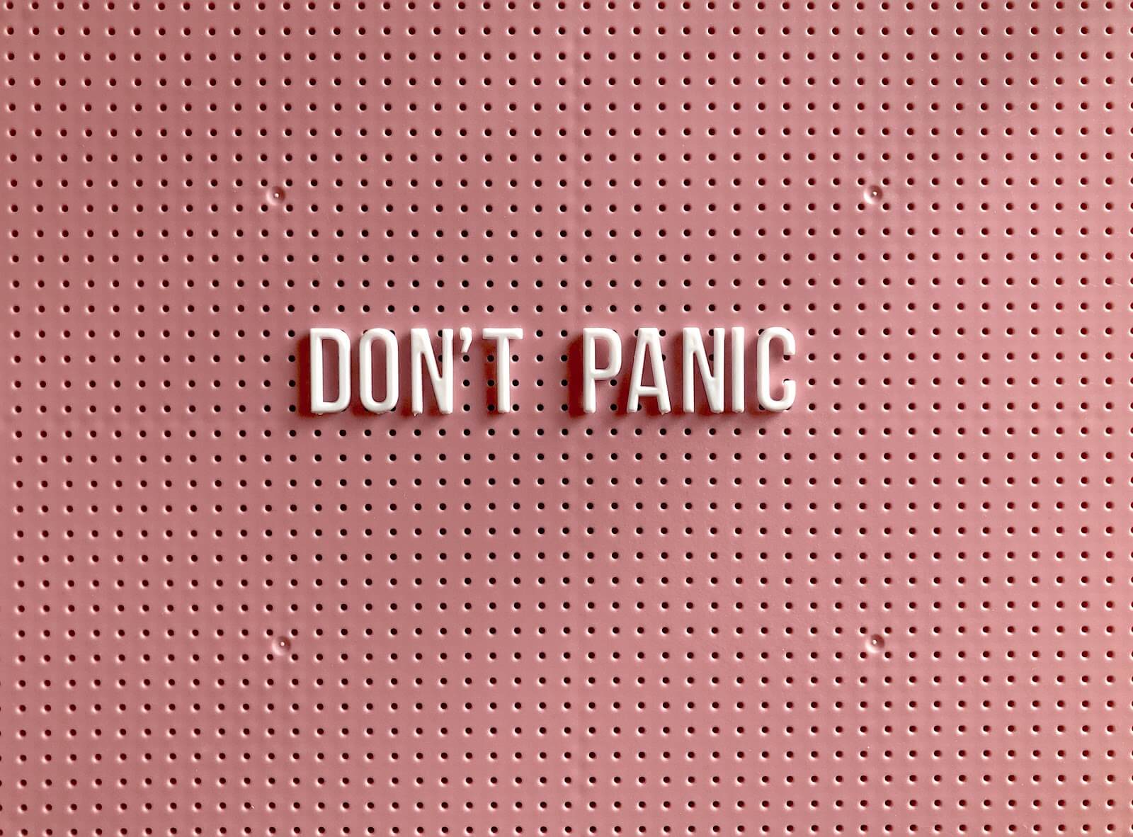 a rose pink metal board with the words "don't panic" in the center